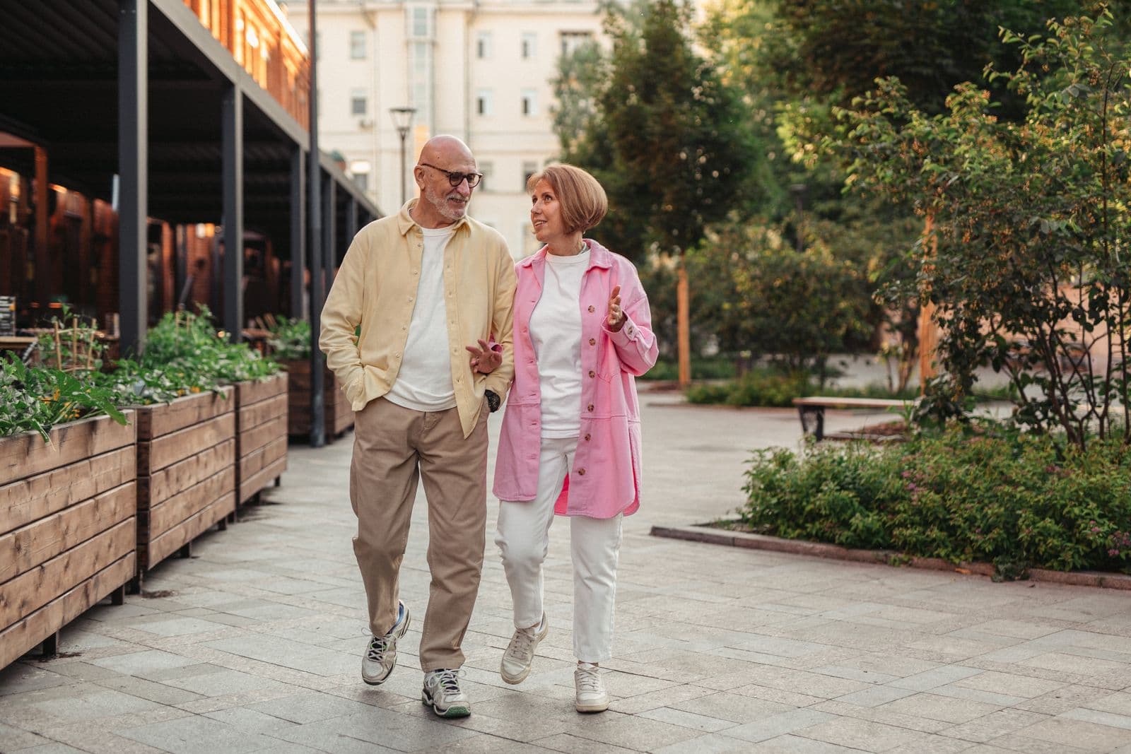 Two adults talking while walking beside planted borders on a sunny pedestrian street