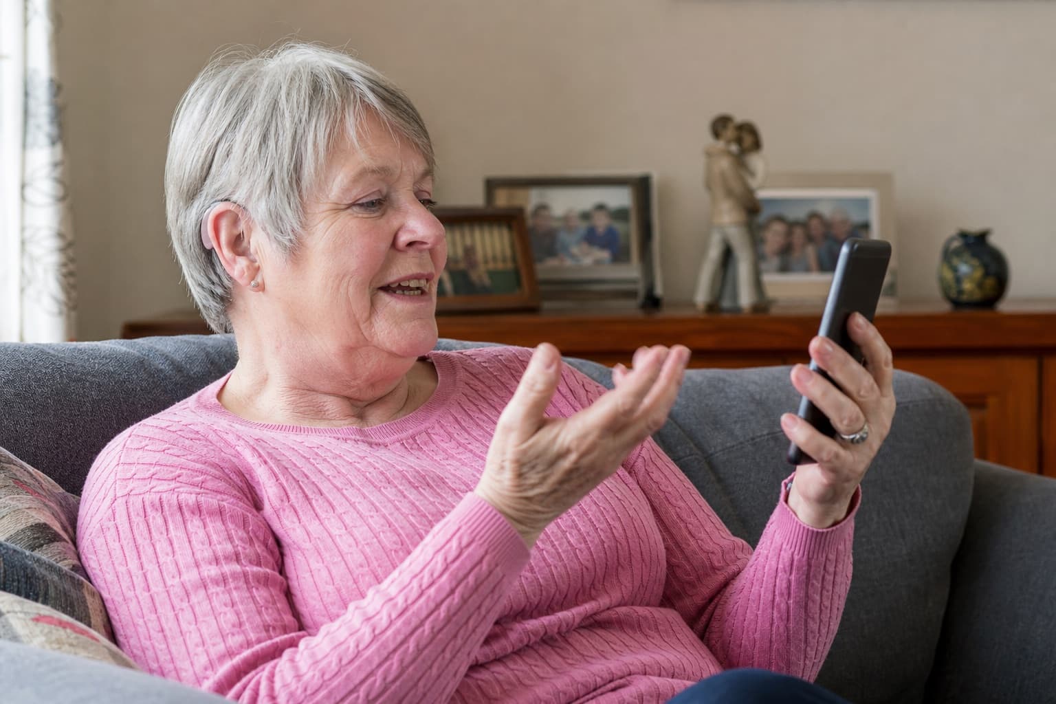 Older woman using her smartphone while wearing discreet hearing aids at home