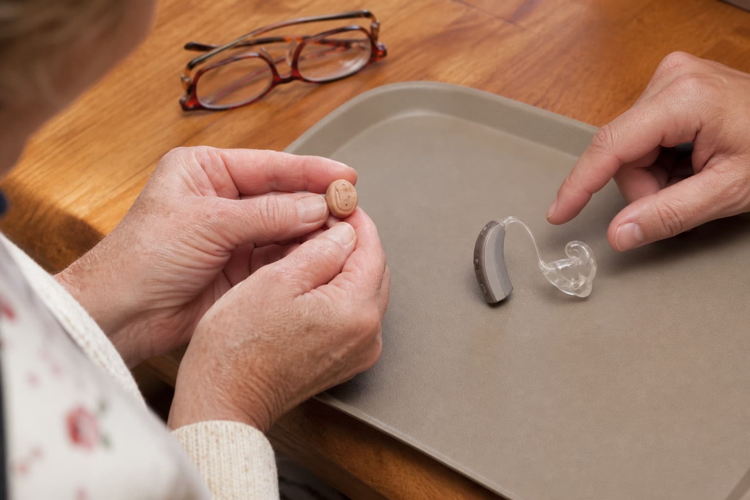 Older adult comparing a custom in-ear hearing aid with a behind-the-ear hearing aid and earmould