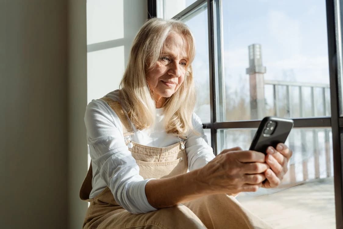 A woman using her smartphone beside a sunlit window at home